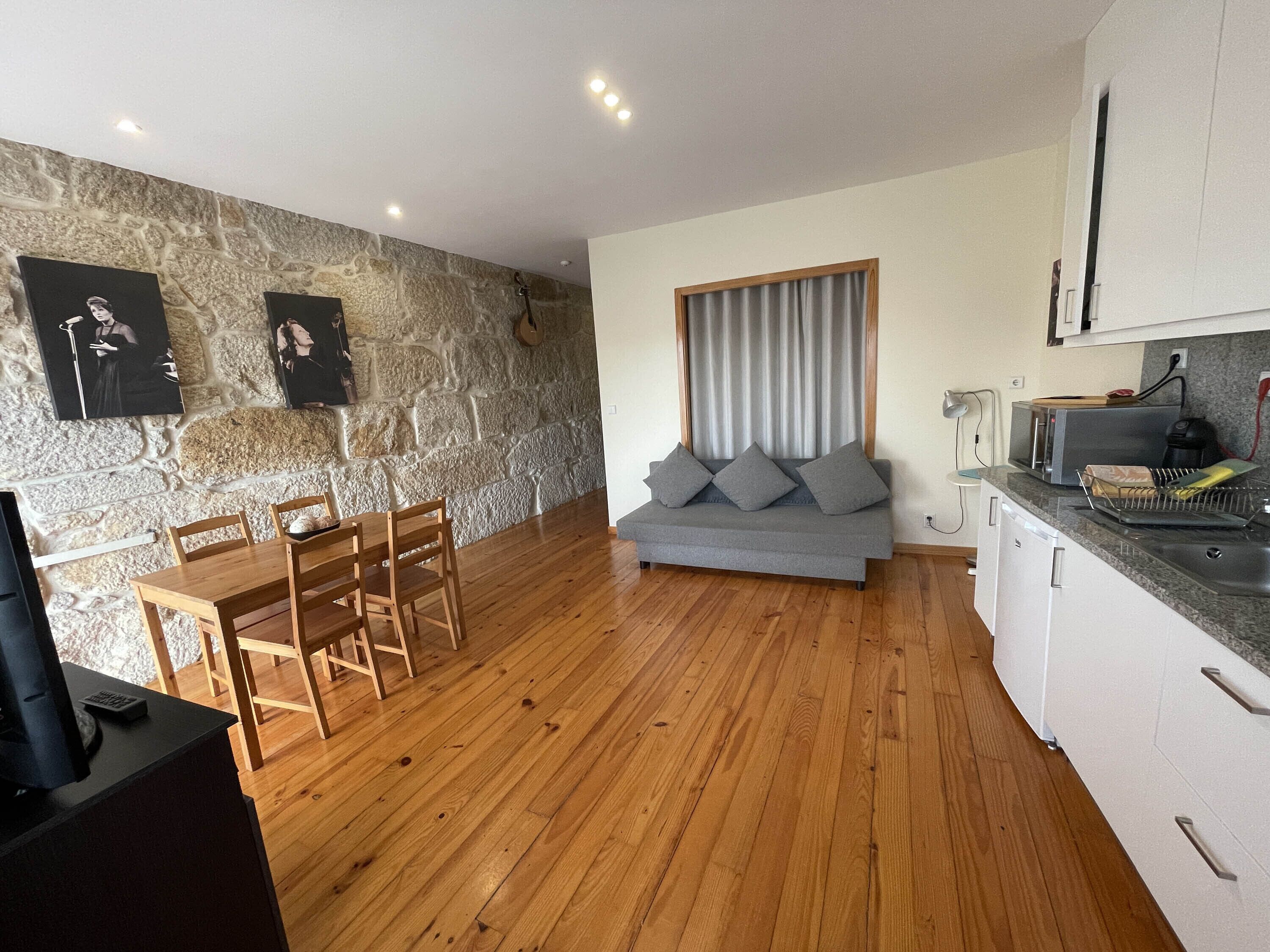 A modern kitchen with a stone wall, wooden dining table, grey sofa, and white cabinets.