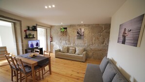 A living room with a stone wall, a sofa, a dining table with chairs, and a television. - Cedofeita Back Garden (Porto)