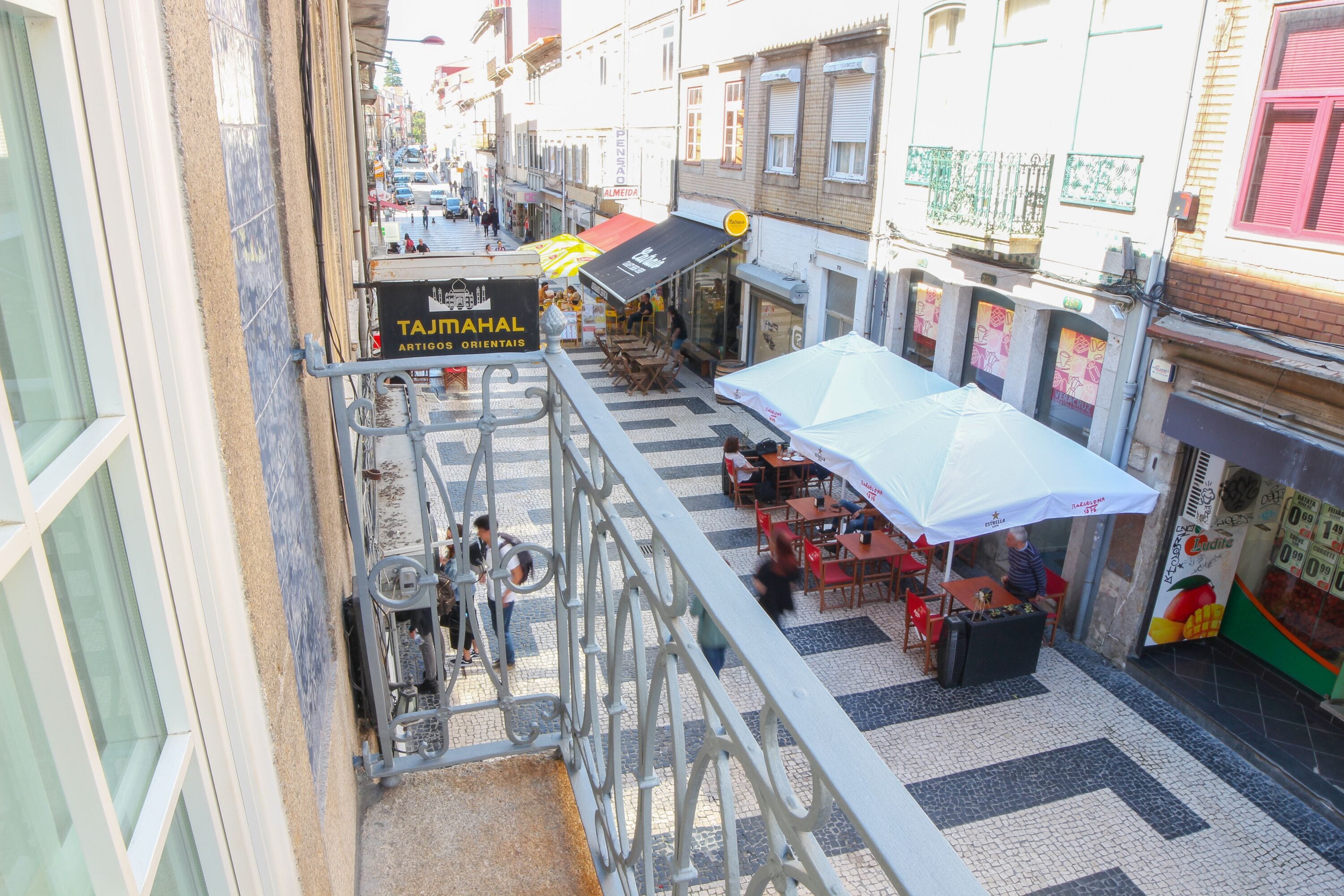 Vista a nivel de calle de un restaurante con mesas al aire libre, un letrero que dice 'Taj Mahal Artigos Orientais', y un pavimento adoquinado.