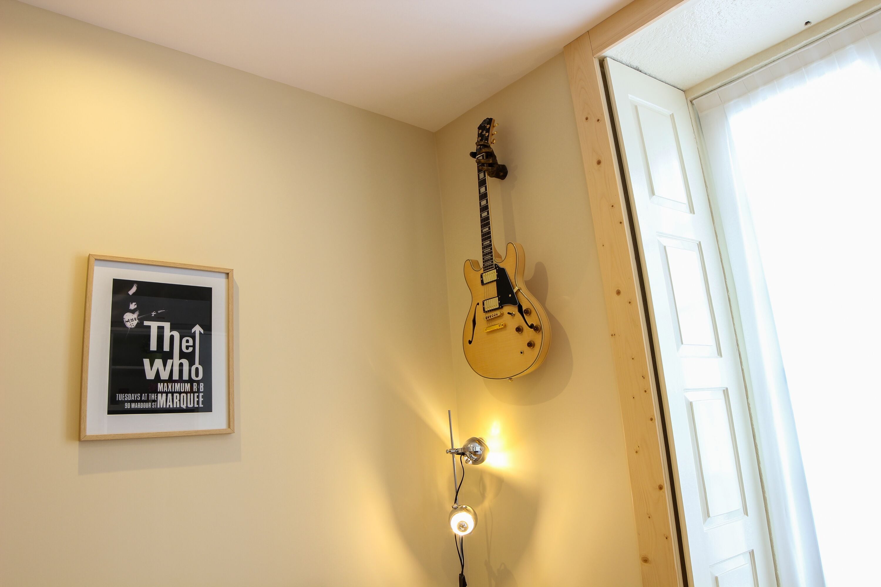 A room with a guitar hanging on the wall, a framed poster, and a door.