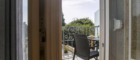 An open door to a balcony with a metal railing, a table with chairs, and a potted plant.