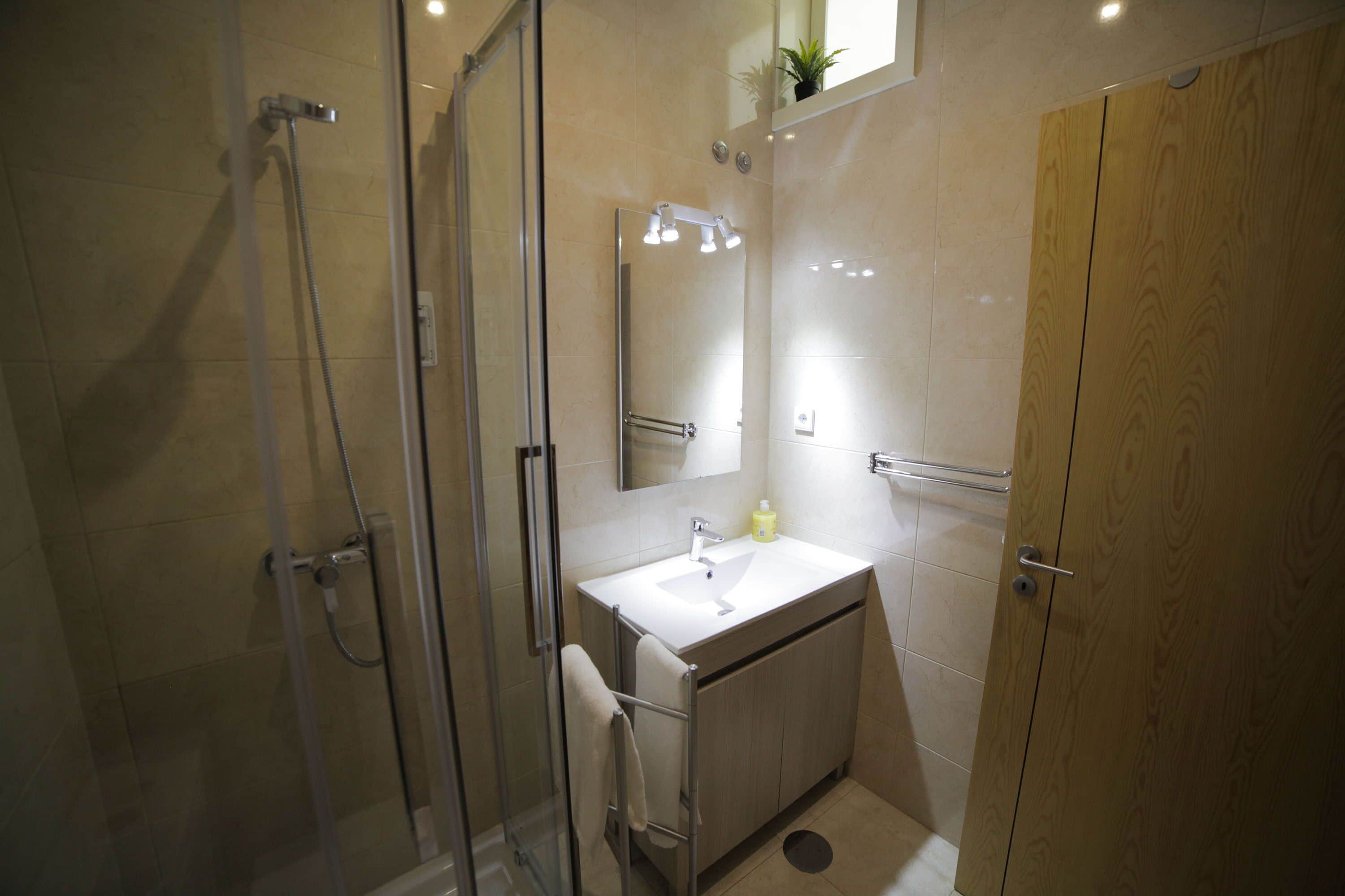 Een moderne badkamer met een douchecabine van glas, een wit wastafelmeubel en een houten kast.