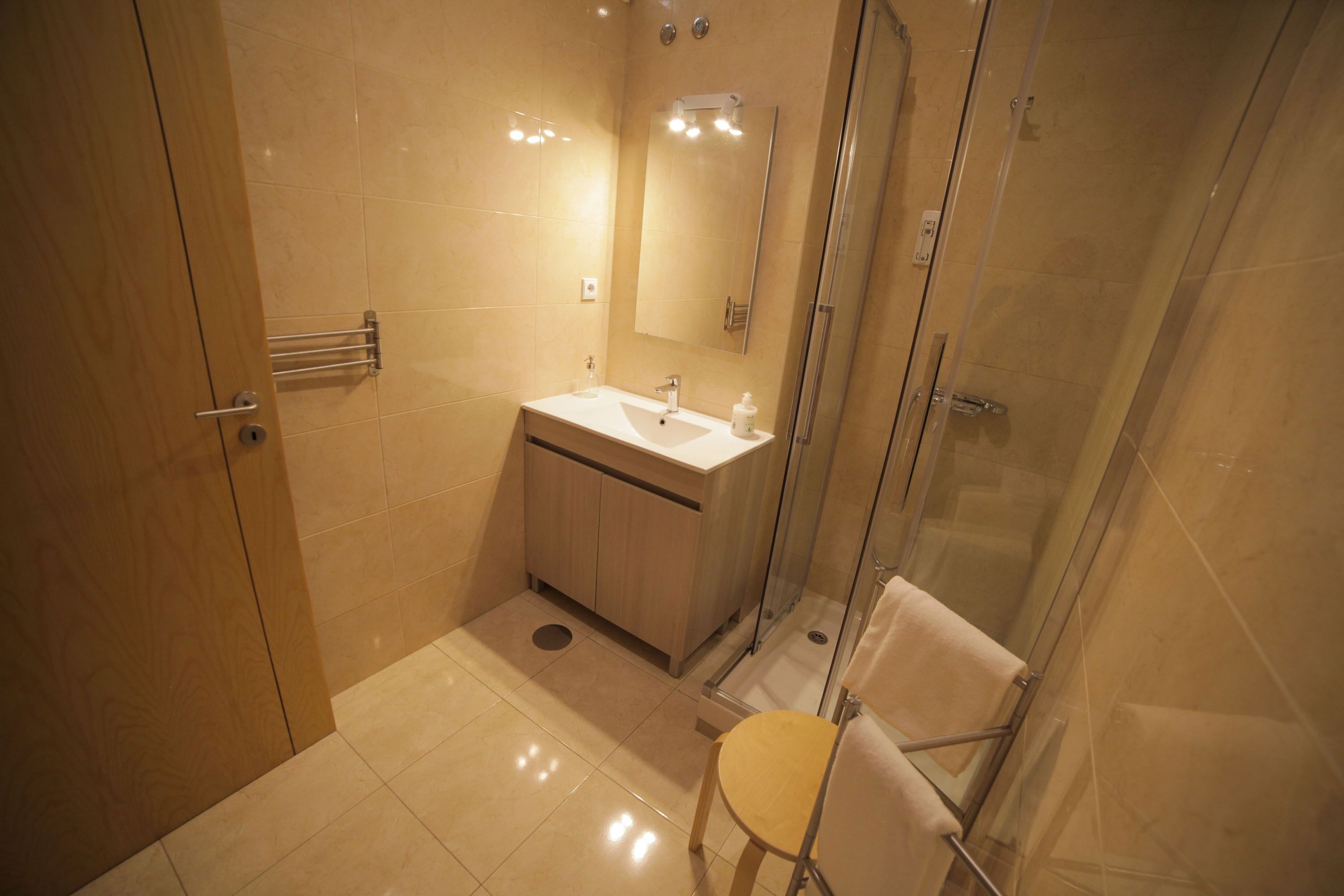 Un bagno moderno con cabina doccia in vetro, mobile bagno in legno e lavandino bianco.