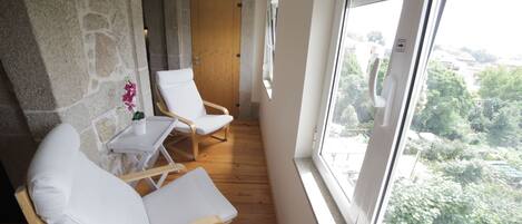 A balcony with two white cushioned chairs, a small table, and a potted plant.