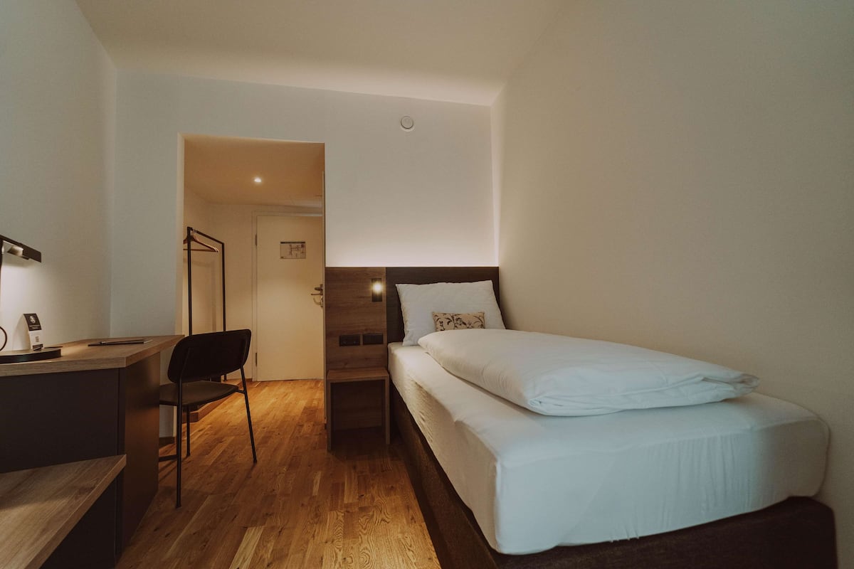 A compact hotel room with a bed, a desk, and a chair.