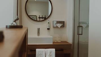 Une salle de bain avec un meuble-lavabo en bois, un miroir rond, un lavabo blanc et une cabine de douche en verre.