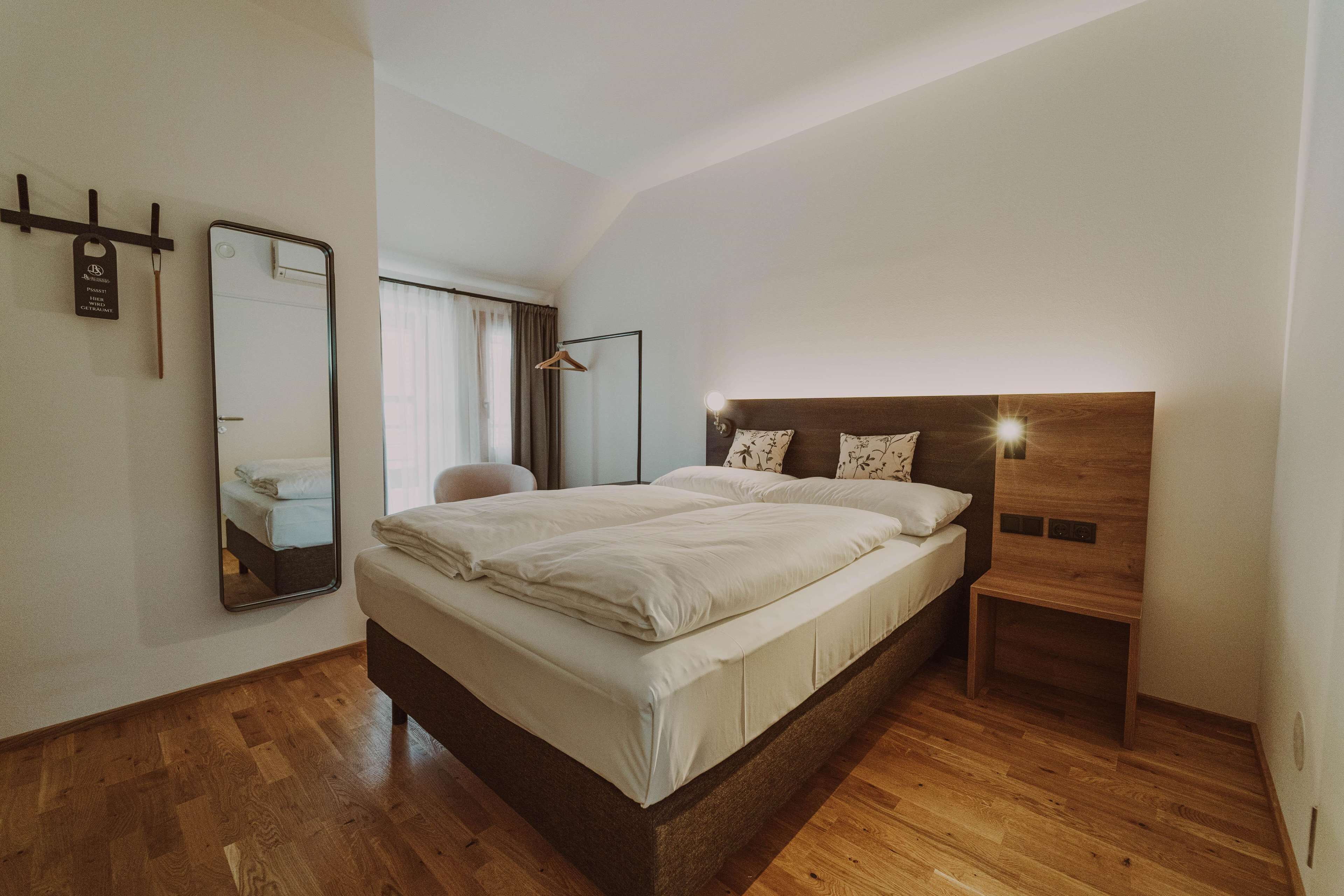 A modern bedroom with a large bed, wooden headboard, bedside tables, and a mirror.