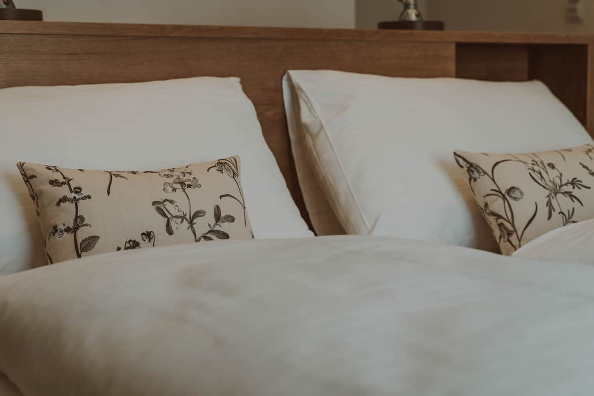 A bed with white bedding and two pillows with a floral pattern.