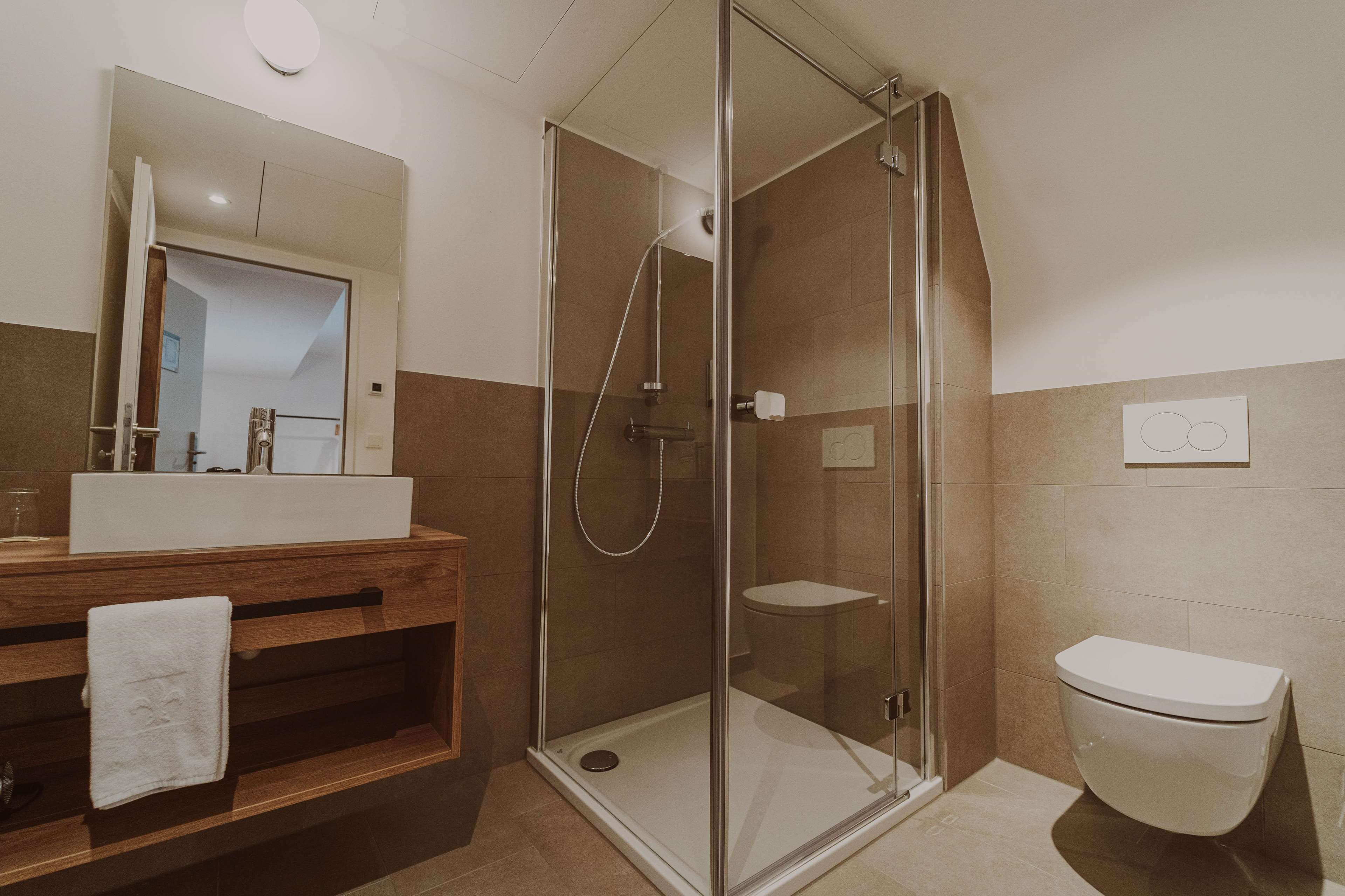 Un baño moderno con ducha envuelta en vidrio, tocador de madera con lavamanos y un inodoro.