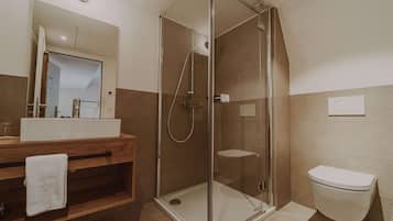 Un baño moderno con ducha envuelta en vidrio, tocador de madera con lavamanos y un inodoro.