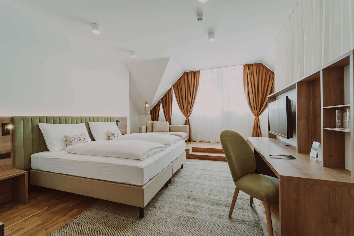 A modern hotel room with a bed, a desk, a chair, and a television.