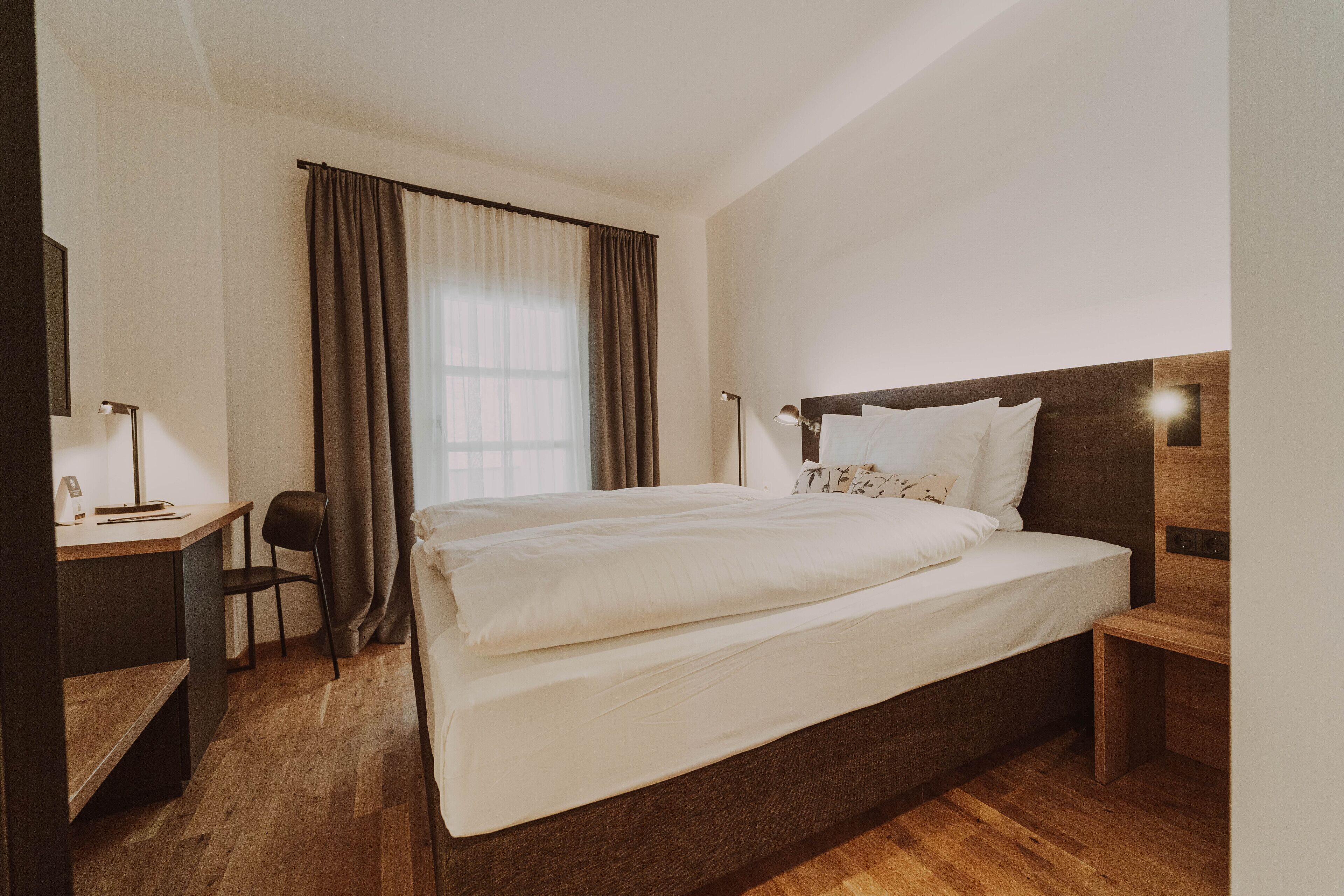 A hotel room with a large bed, a desk, a chair, and a nightstand.