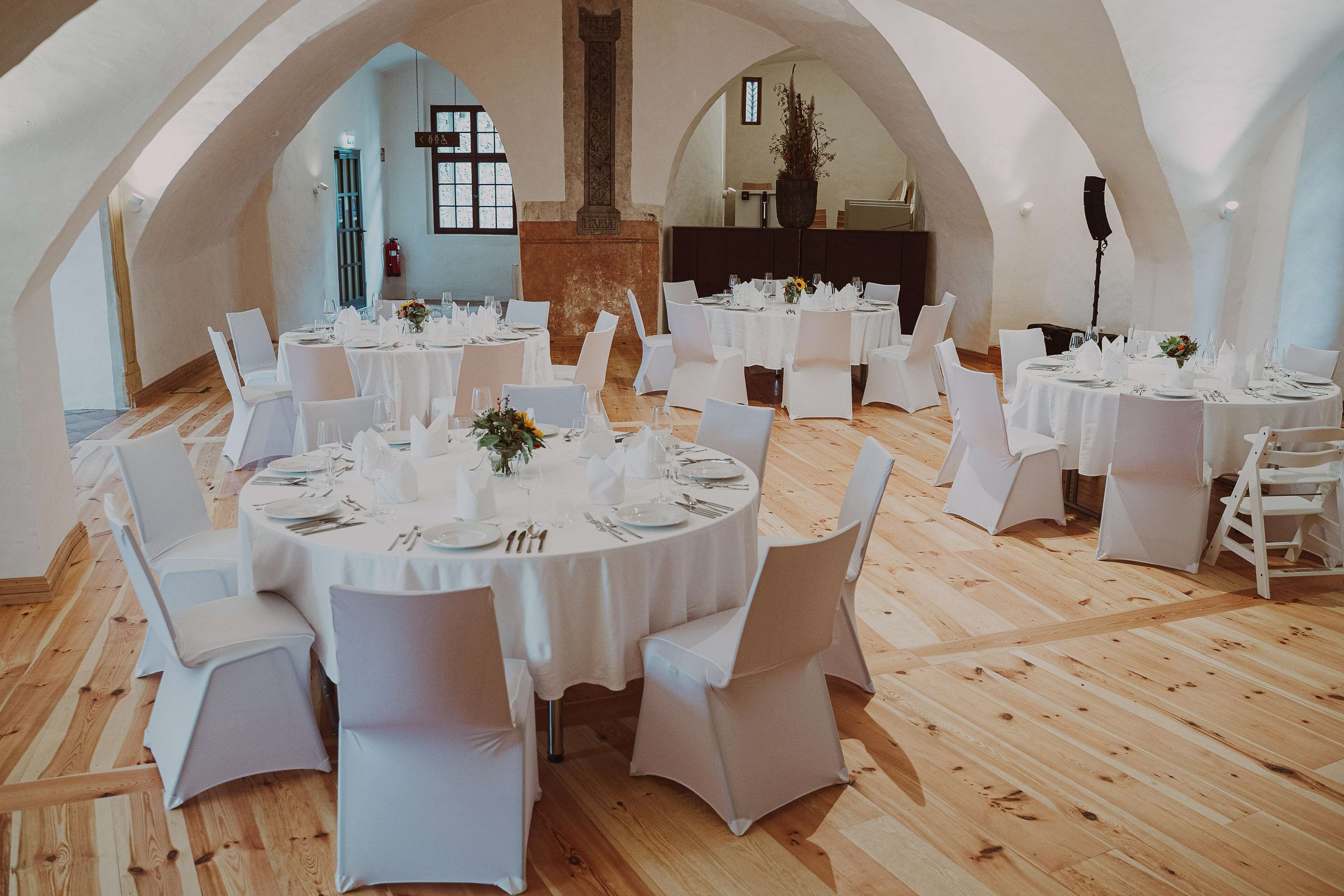 Una ampla sala de dinar amb taules rodones, tovallons blancs i cadires blanques.