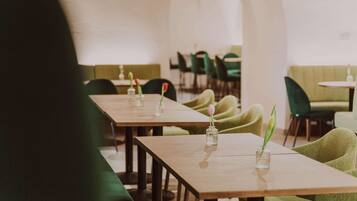 Un restaurante con mesas de madera largas, sillas tapizadas de verde y jarrones con flores.