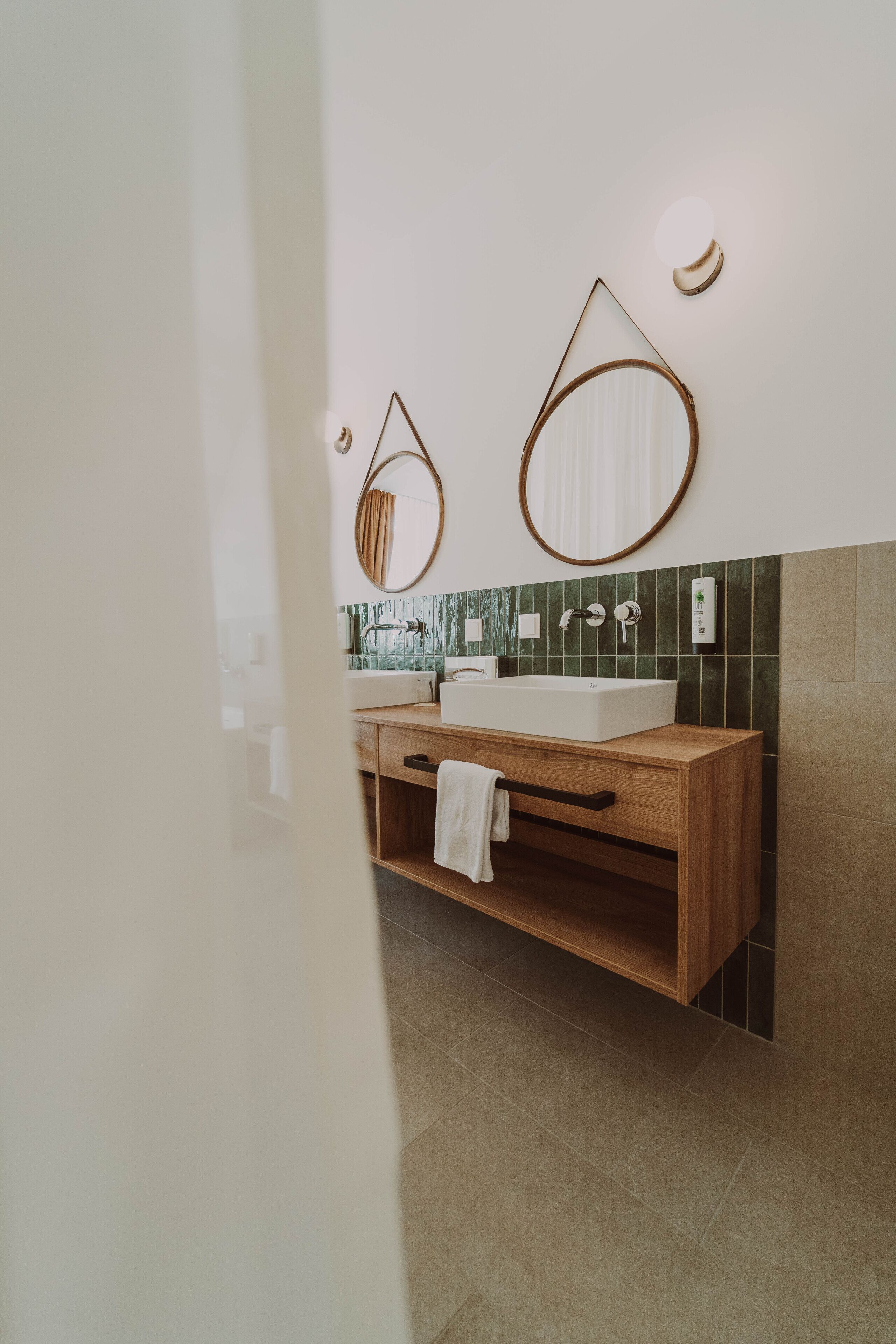 A modern bathroom with a wooden vanity, a large mirror, and a wall-mounted light fixture.