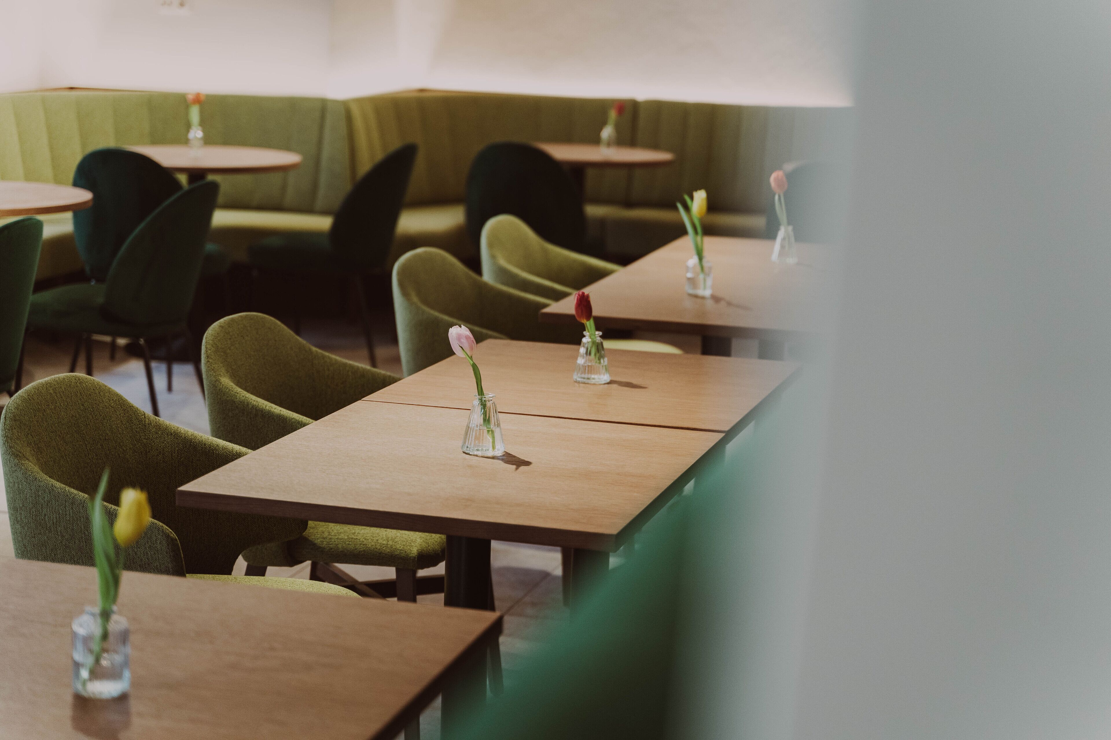 A restaurant with green upholstered booths and wooden tables, each with a small vase of flowers.