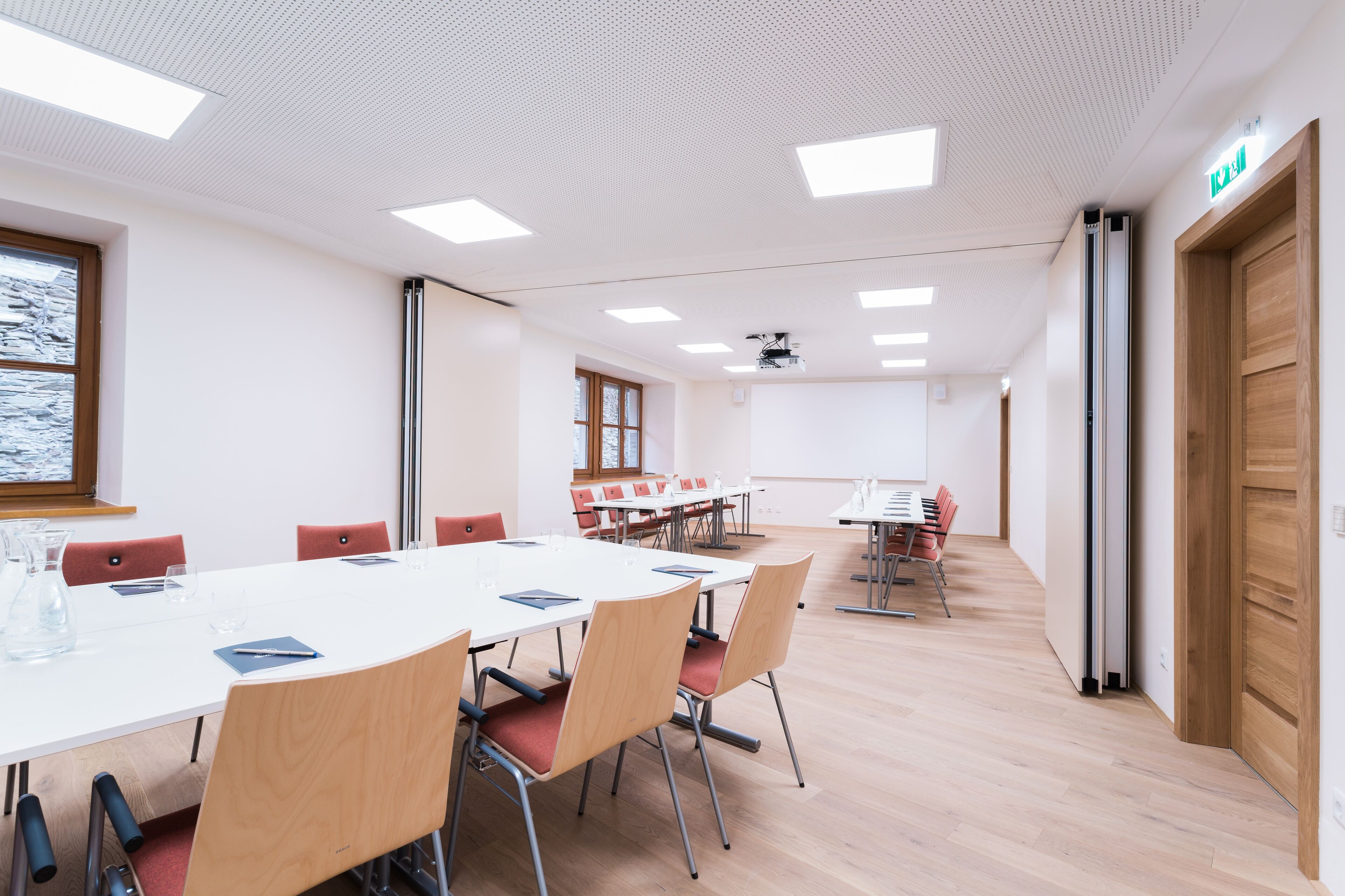 Une salle de conférence avec une table blanche, des chaises rouges et un écran de projection.