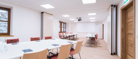 A conference room with a white table, red chairs, and a projector screen.