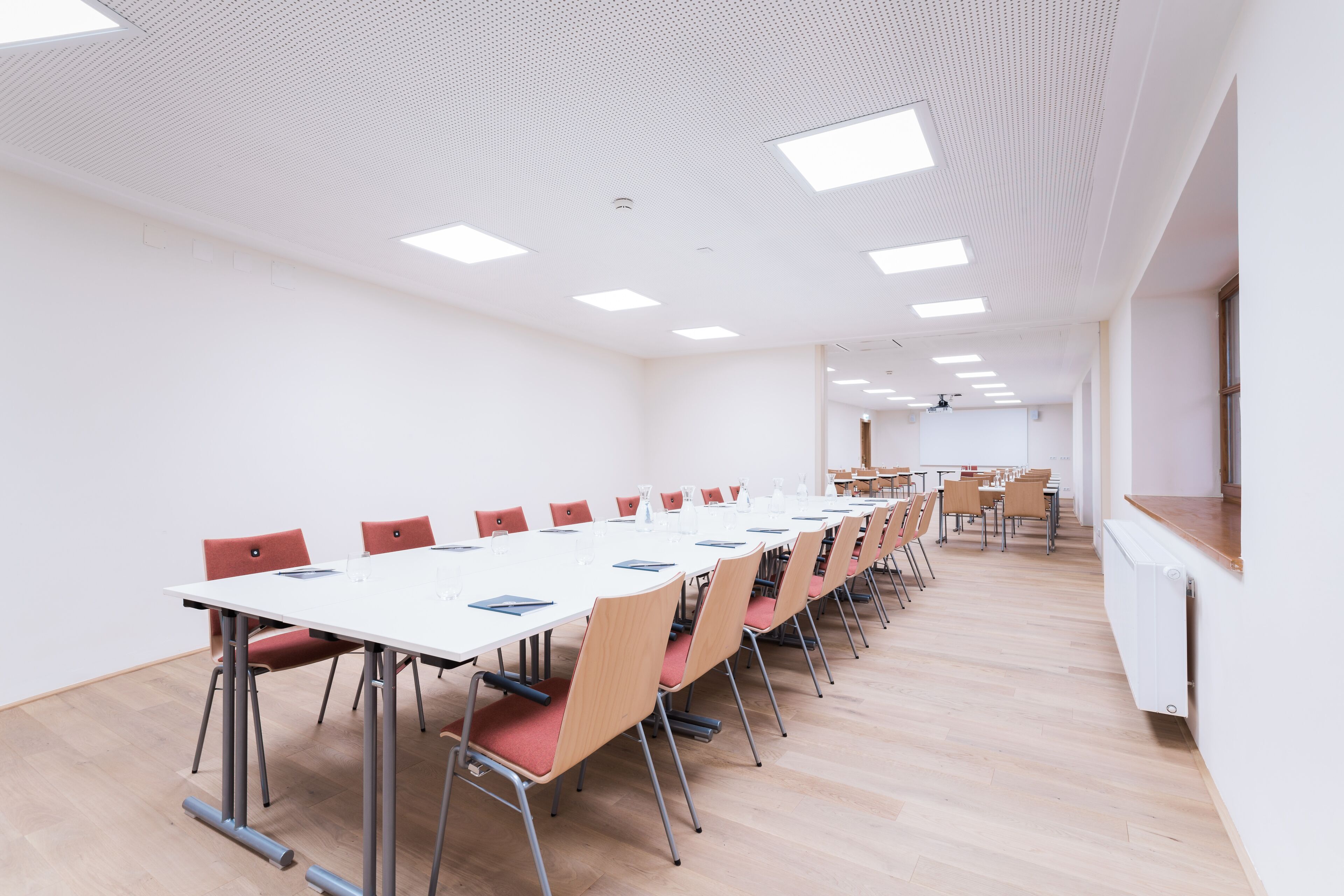 A conference room with a long table, red chairs, and a whiteboard.