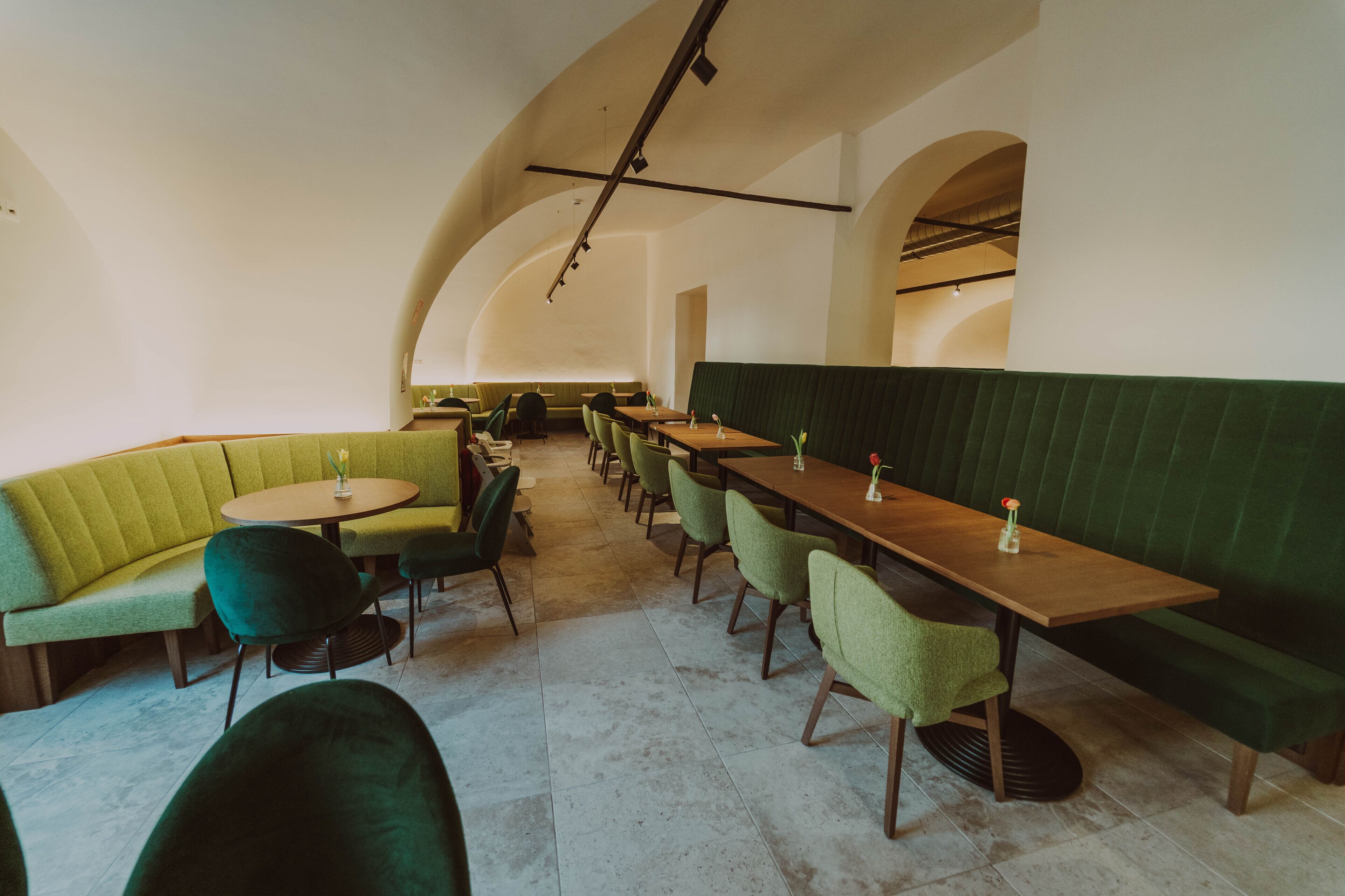 Restaurante com assentos estofados em verde, mesas de madeira e teto alto com vigas aparentes.