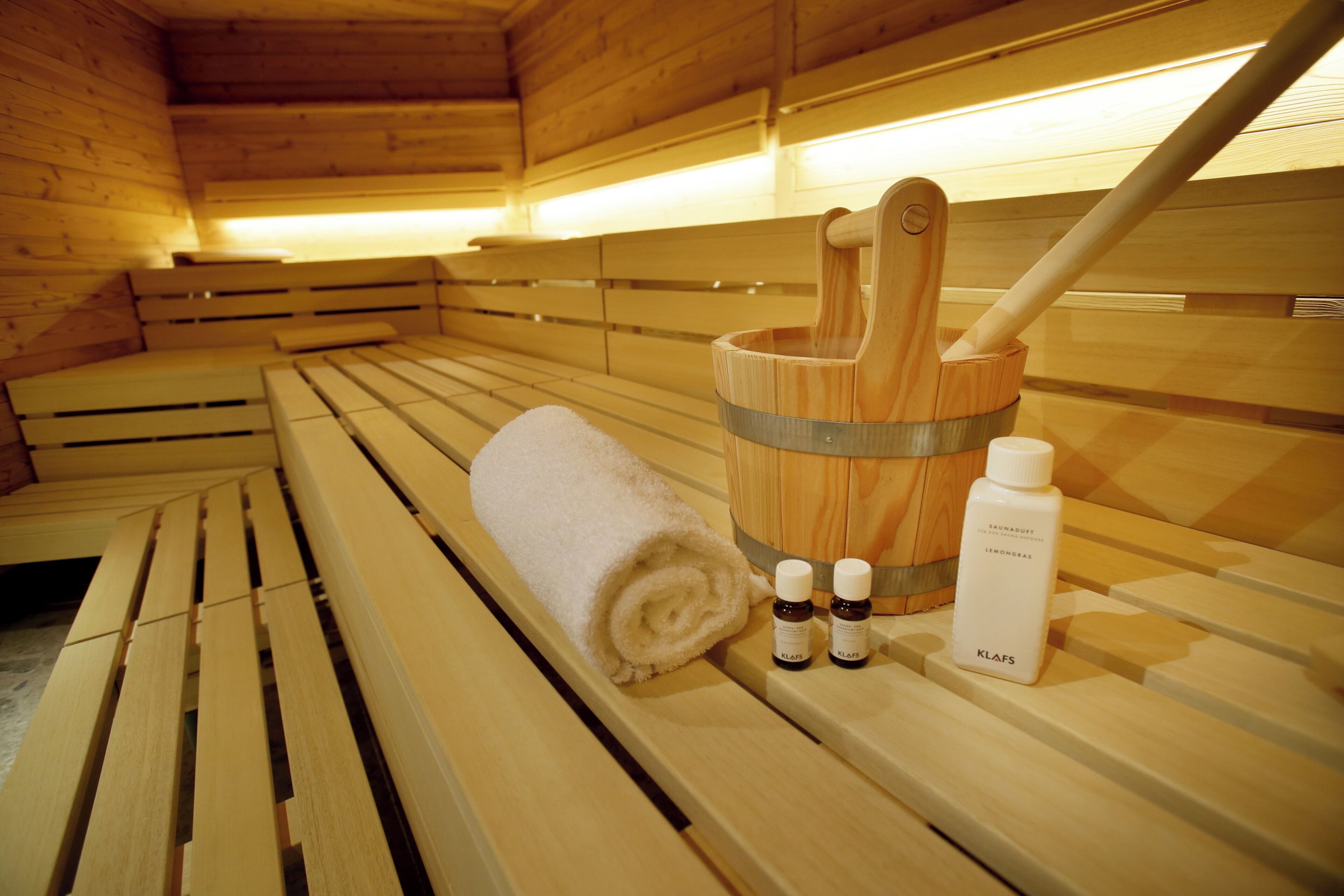 A wooden sauna bench with a rolled towel and a wooden bucket with a brush.