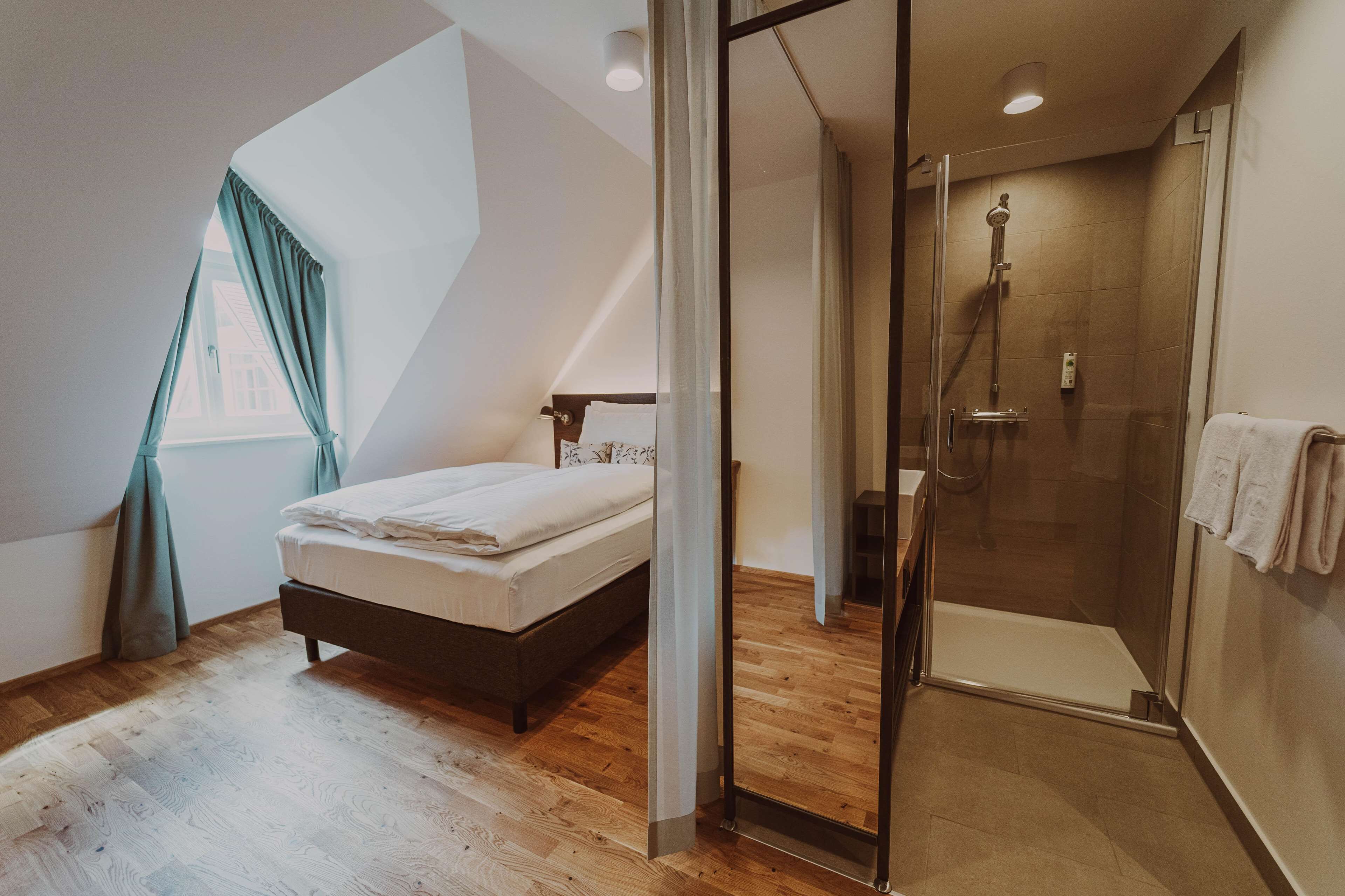 Une chambre avec un lit, un espace douche doté d’une porte en verre et une fenêtre avec des rideaux.