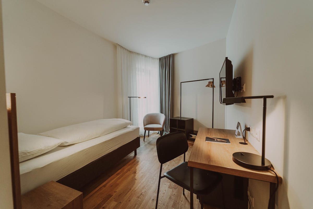 A room with a bed, a desk, a chair, a lamp, and a television.