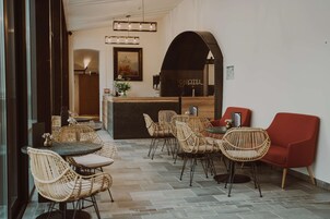 Un hall de hotel con sillones de mimbre, un sillón rojo y una mesa de recepción.