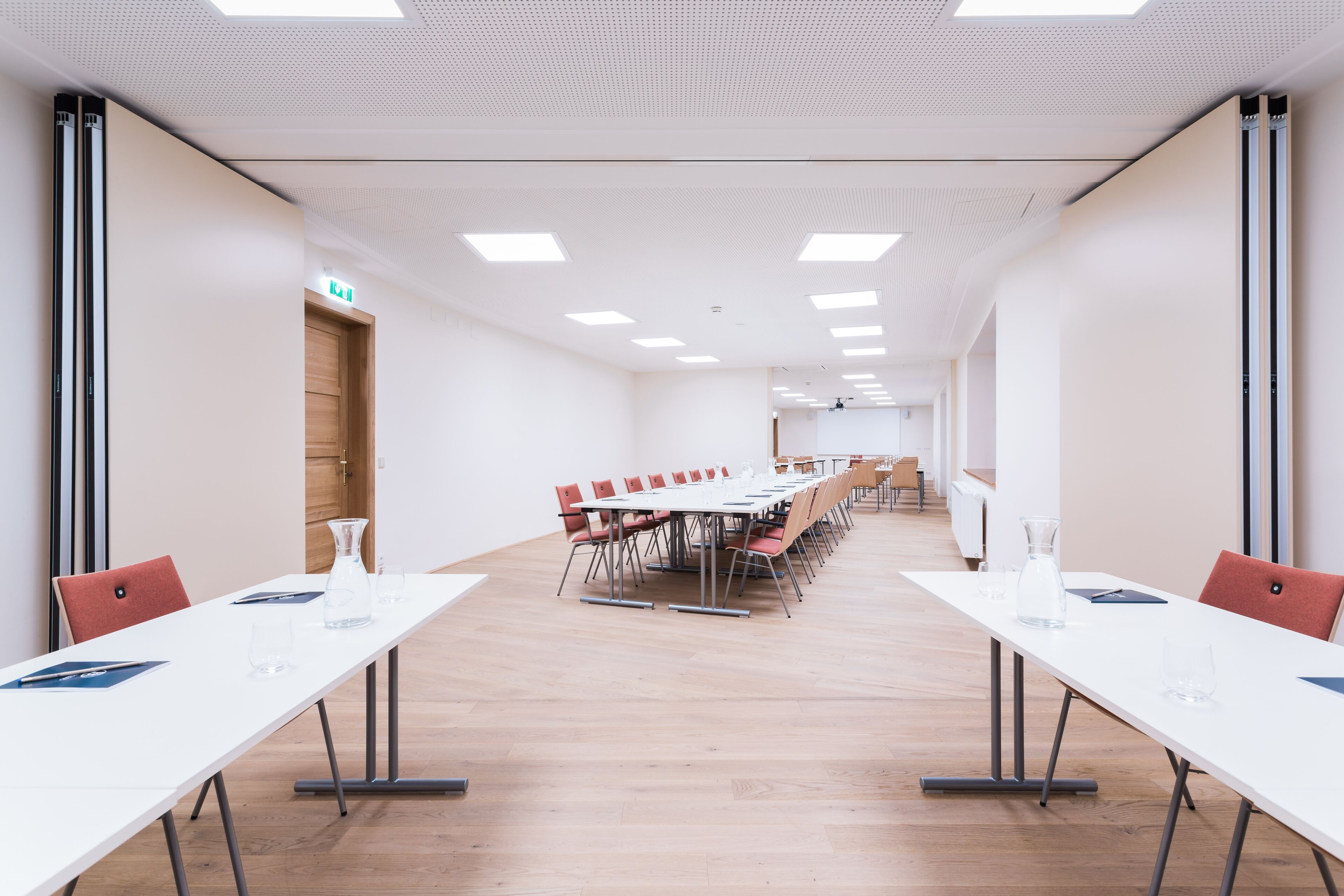A conference room with a long table, chairs, and a wooden floor.