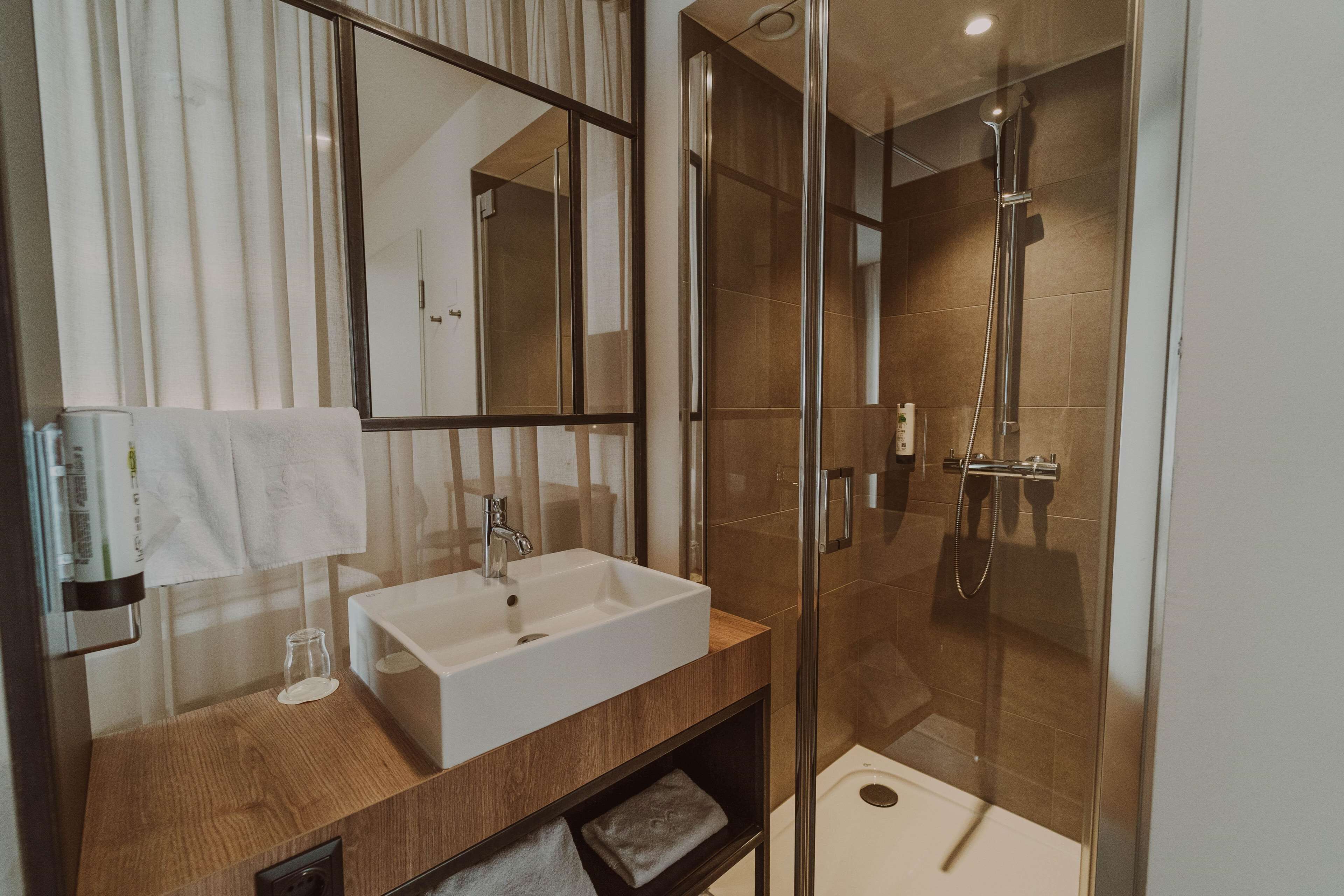 A modern bathroom with a wooden vanity, a large mirror, a white sink, and a glass-enclosed shower.