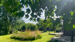Un jardin bien entretenu, agrémenté d’une terrasse, et entouré d’une végétation luxuriante et d’arbres.