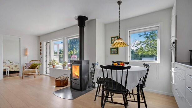 Une cuisine moderne dotée d’un poêle à bois, de meubles blancs et d’un coin repas avec une table et des chaises.
