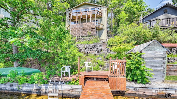 A wooden dock leading to a house with a balcony, surrounded by lush greenery. - Waterfront Glen Lake Cabin w/ Boat Dock & Deck (Queensbury)