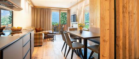 A modern kitchen with a dining area, wooden ceiling, and large windows offering a view of greenery.