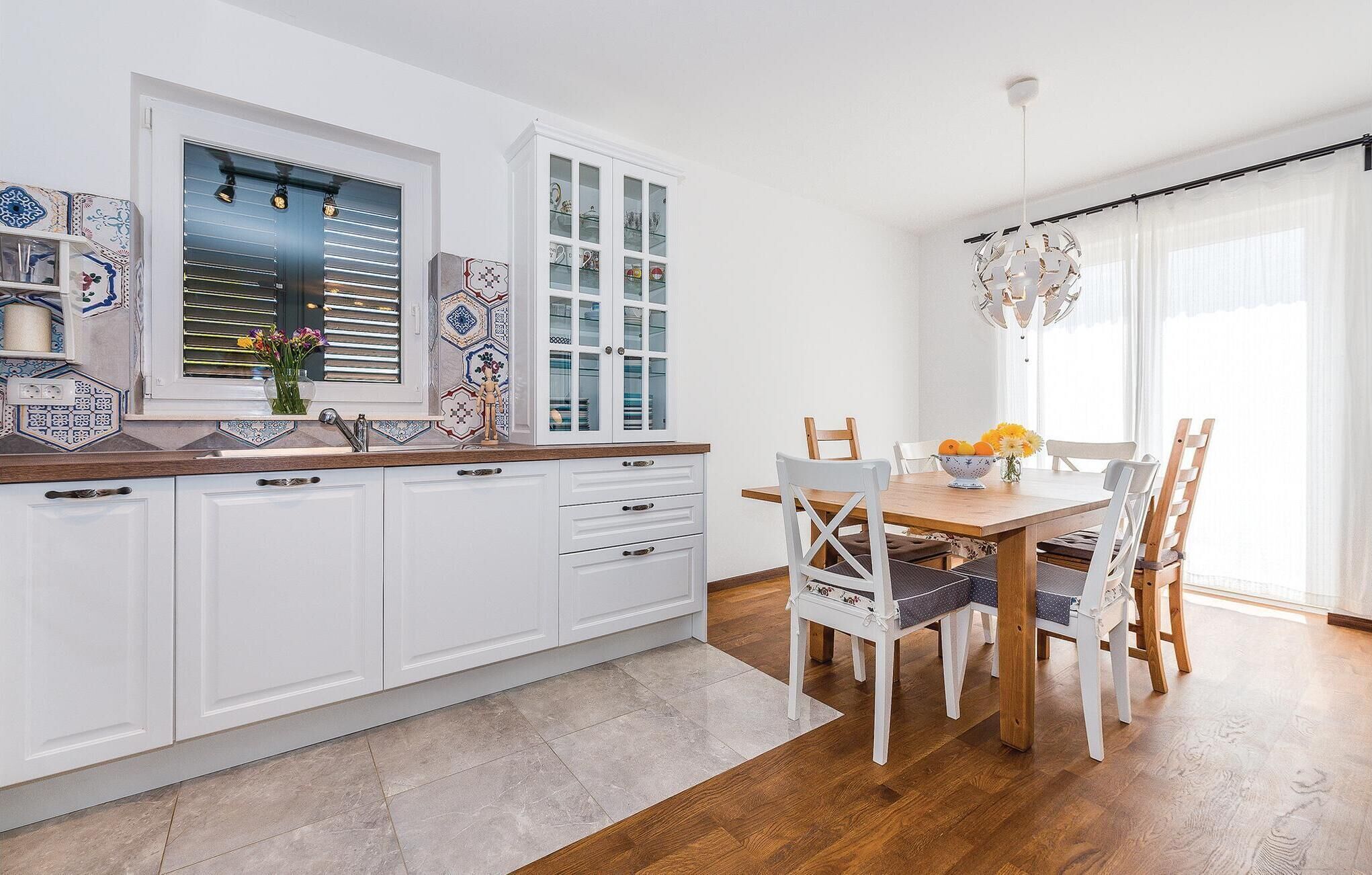 A modern kitchen with white cabinets, a wooden countertop, and a dining area with a wooden table and chairs.