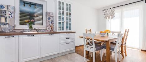 A modern kitchen with white cabinets, a wooden countertop, and a dining area with a wooden table and chairs.