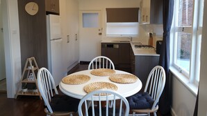 A modern kitchen with a round dining table, white chairs, and a built-in stove. - Winston Cottage Leura - BEST Location & Views (Leura)
