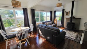 A modern living room with a fireplace, wooden flooring, and large windows with curtains. - Winston Cottage Leura - BEST Location & Views (Leura)