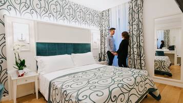 A hotel room with a large bed, a bedside table with a plant, a mirror, and a patterned wall.