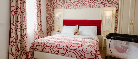 A neatly arranged bedroom with a red headboard, a bed with a patterned bedspread, a nightstand with a lamp, and a Mickey Mouse crib.