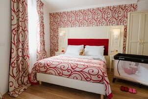 Un dormitorio ordenado con cabecera roja, cama con cubrecama estampado, mesita de noche con lámpara y cuna de Mickey Mouse.