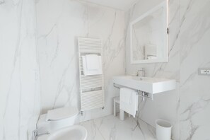 Une salle de bain moderne avec un sol en marbre blanc, un lavabo blanc, des toilettes et un miroir.