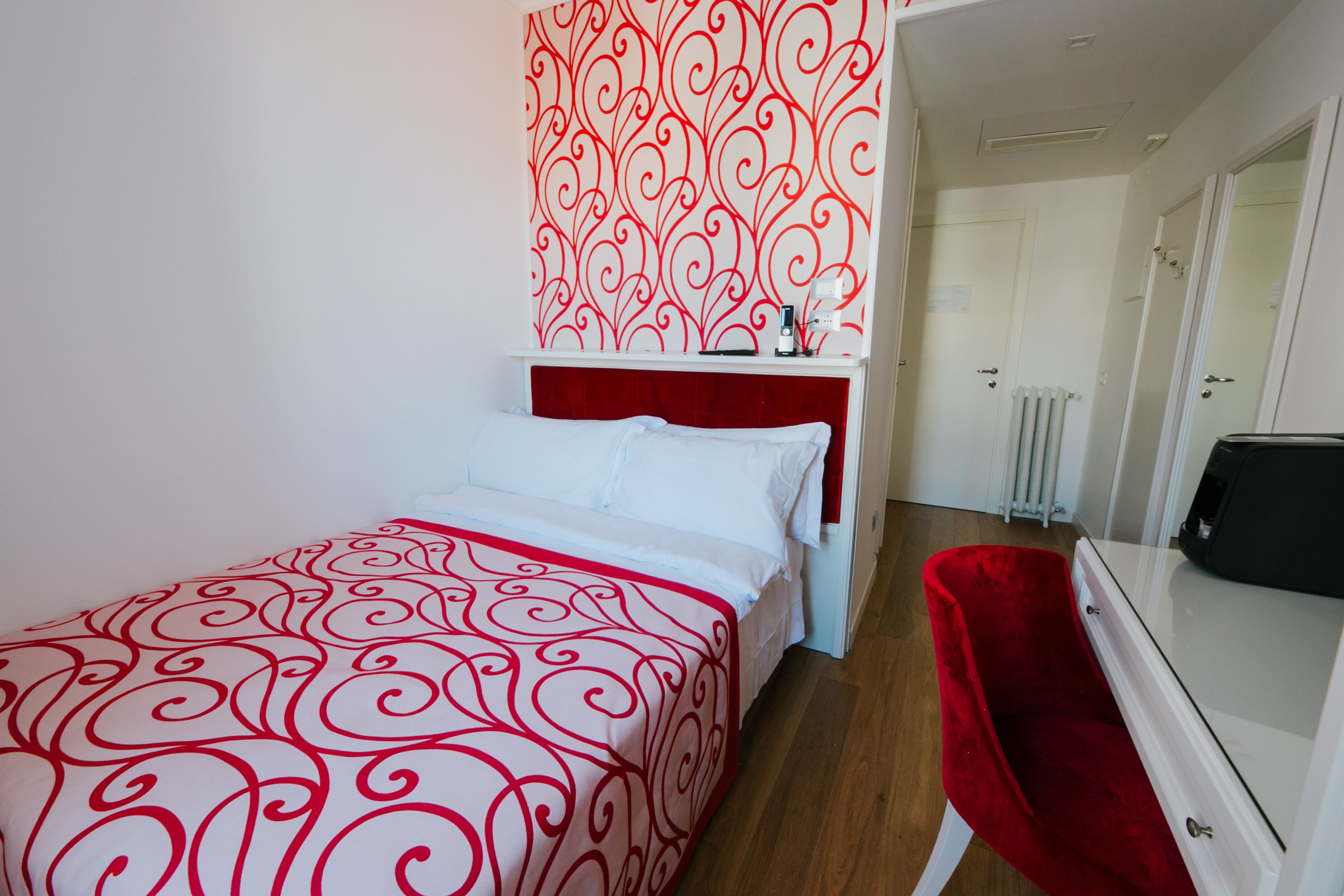A hotel room with a bed, a red chair, a dresser, and a radiator.