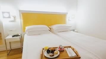 Quarto de hotel com uma cama, um tabuleiro com itens de pequeno-almoço e uma mesa de cabeceira com uma lâmpada.