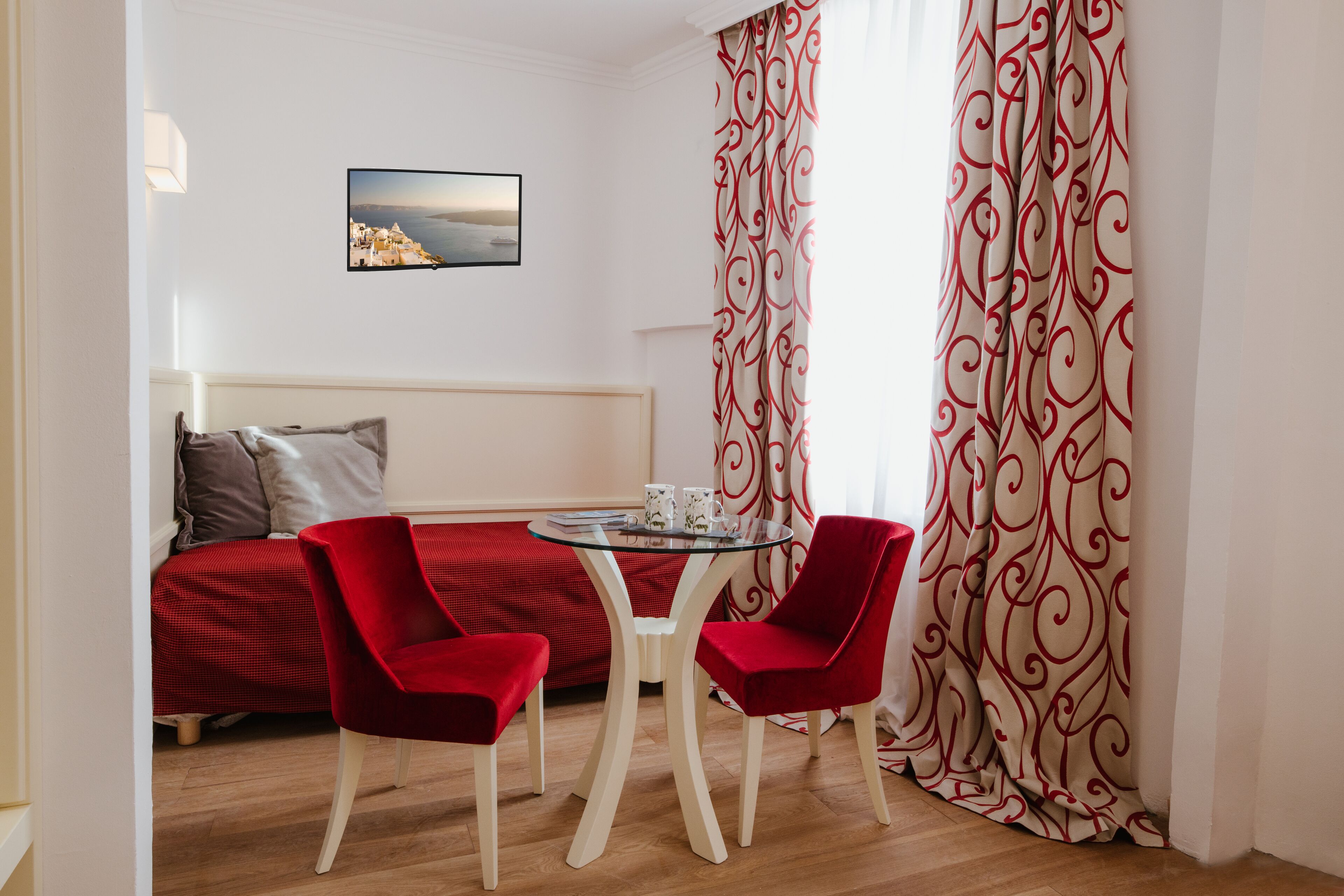 Une pièce avec un lit, deux chaises rouges, une petite table avec des tasses et un tableau accroché au mur.
