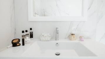 Un baño con lavamanos de mármol blanco, un espejo y diversos artículos de aseo.