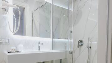 A modern bathroom with a glass-enclosed shower, a large mirror, and a white sink.