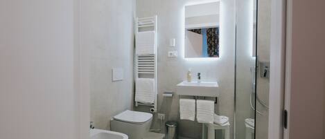 A modern bathroom with a toilet, bidet, sink, and glass shower enclosure.