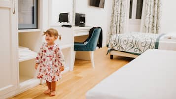 A child in a floral dress standing in a room with a bed, a desk, and a wardrobe.