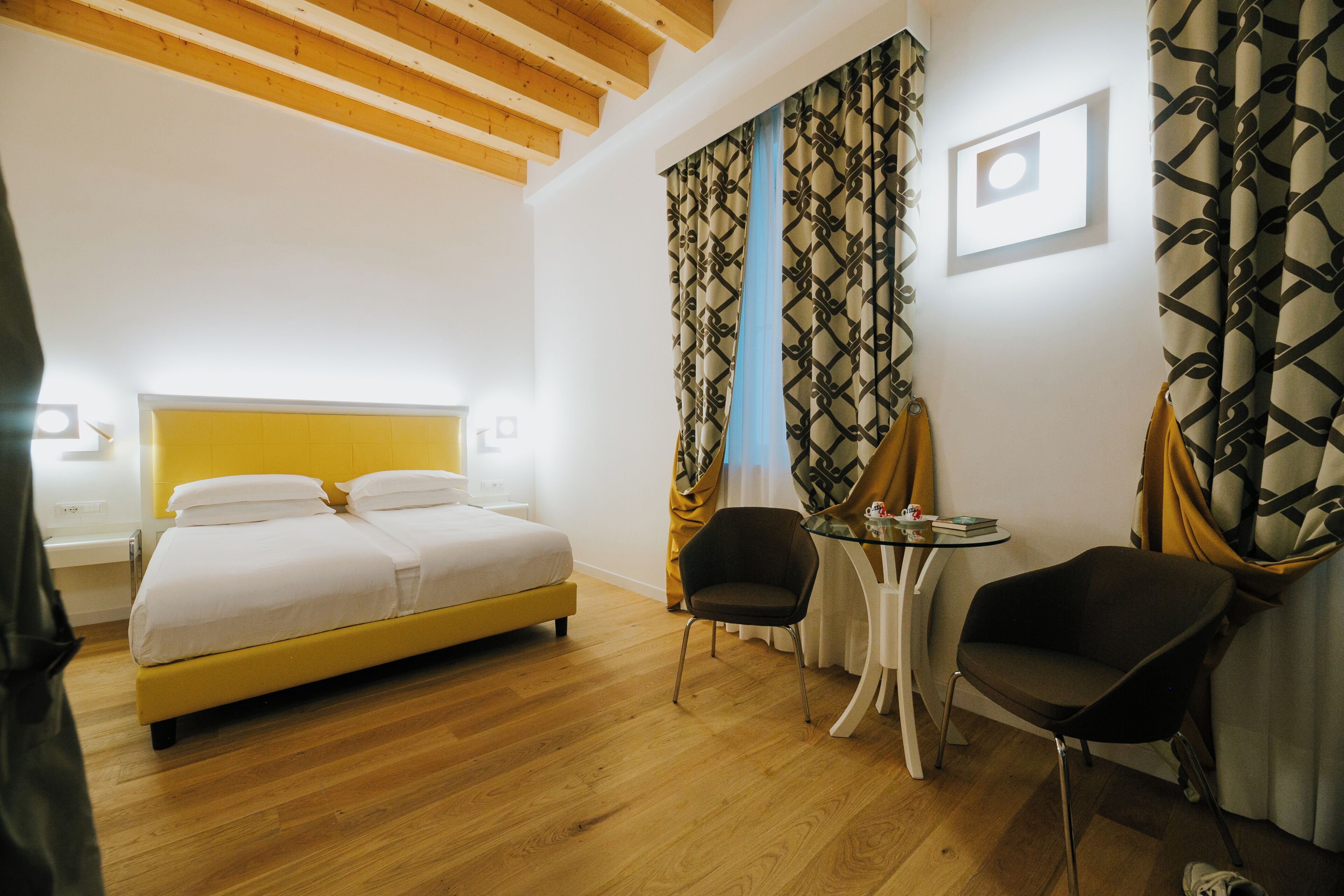 A hotel room with a bed, two chairs, a small table, and a window with curtains.